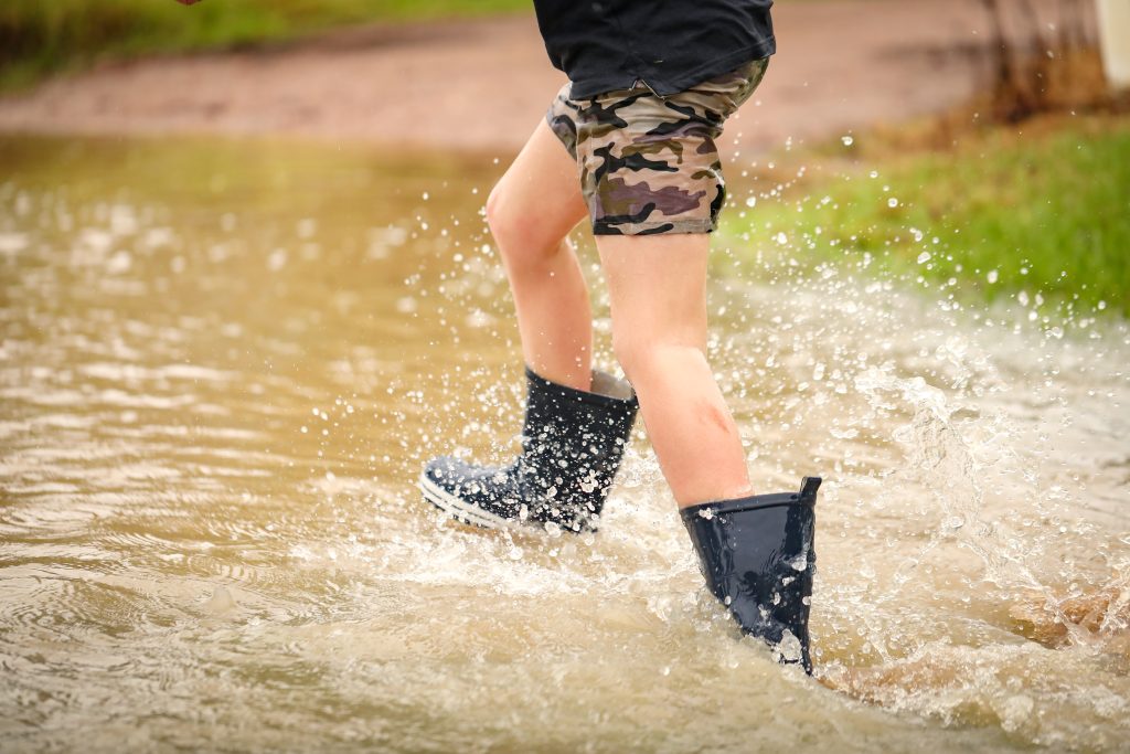 Boy walking through flooded creek wearing gumboots